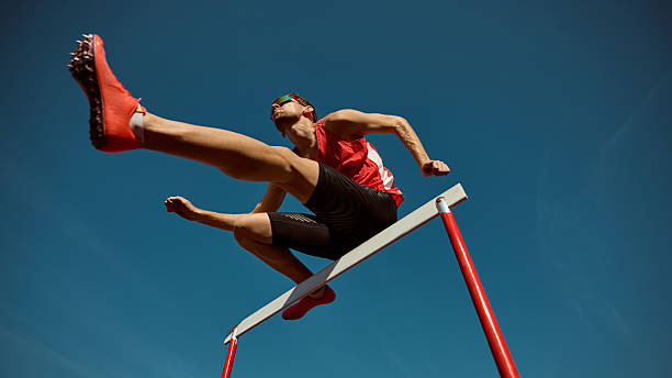 Athlete in red leaping over hurdle with power and confidence under clear sky