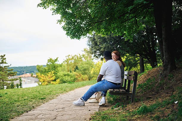 istock Young couple sitting on a park bench enjoying nature 2242775962