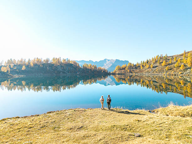 istock Two Hikers Standing by Mountain Lake Reflection 2242778353
