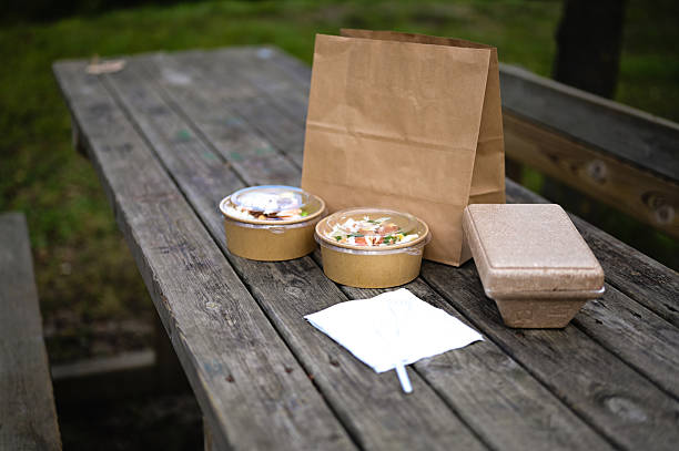 Takeout food containers with a paper bag sitting on a wooden picnic table