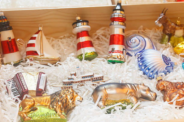 Beautiful Christmas tree balls made of glass in designs of Lighthouses, Shells, Steamboat, Sailing Ship, Hippopotamus, Lion, Goat, Squirrel and an Accordion, at a display of a booth at a Christmas market.
