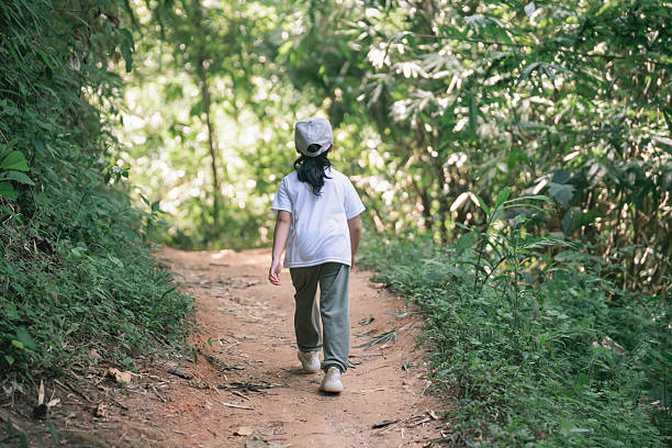 Child Walking on Dirt Path Through Lush Green Forest Surrounded by Trees and Vegetation during Daytime Sunshine in Nature Adventure Playtime