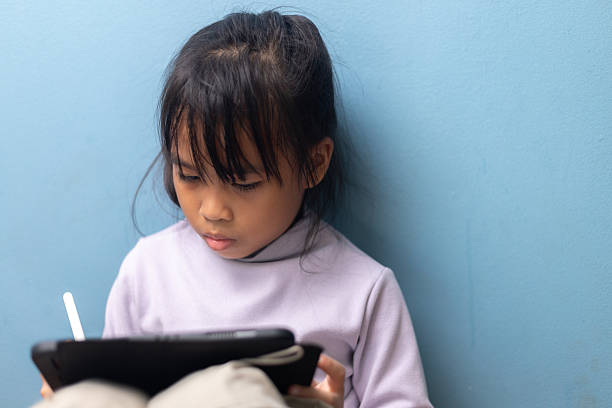 istock Asian little girl using tablet with stylus and focusing on study on blue wall background, concept of digital education, smart learning, e-learning, and technology for kids. 2242792479