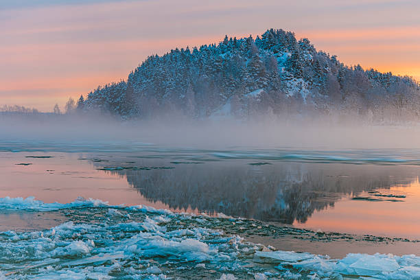 A serene winter morning along the Bow River in Calgary, Alberta, where mist rises from partially frozen waters. The scene captures the quiet resilience of nature in deep winter.