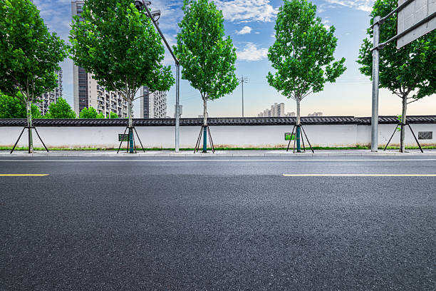 istock Empty asphalt road next to a white wall with a row of green trees. 2242796131