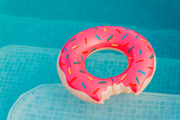 istock Pink donut pool float in a refreshing blue swimming pool on a sunny day. 2242814192