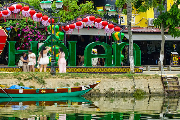 Colorful traditional Vietnamese houses, streets and boats decorated with lanterns on the riverbank, with unrecognizable people, in honor of the lantern festival in Hoi An, Vietnam, 2025