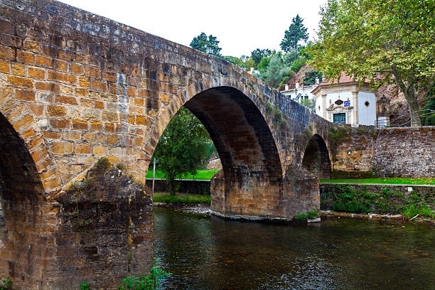 istock An ancient stone arch bridge spans a calm river, flanked by lush greenery 2242817045