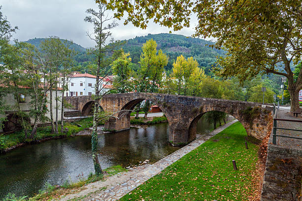 istock An ancient stone arch bridge crosses a tranquil river in a charming village, framed by autumnal trees and backed by verdant, forested hills 2242818139