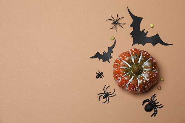 istock Elegant Halloween decor. Top view capturing thematic elements: small orange and golden pumpkins, insects, scary spiders, cobwebs, bats. Empty space for greetings or promotions. 2242819497