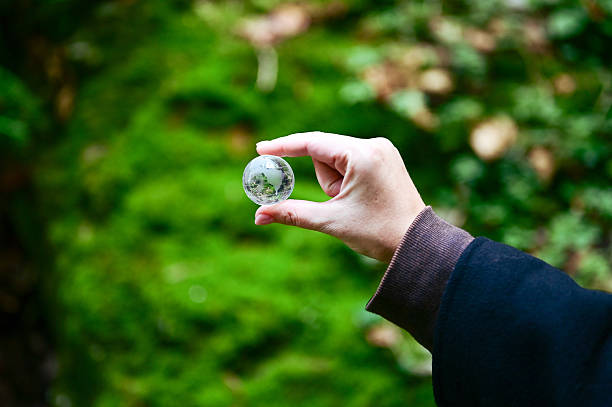 Hand holding a small glass globe in front of a green nature background