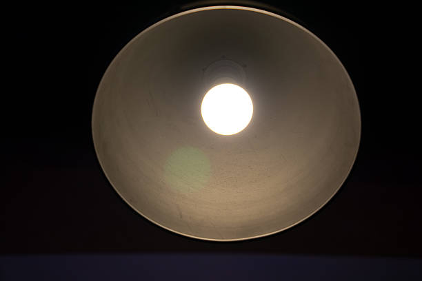 A glowing light bulb inside a metallic lampshade, viewed from directly below against a dark background.