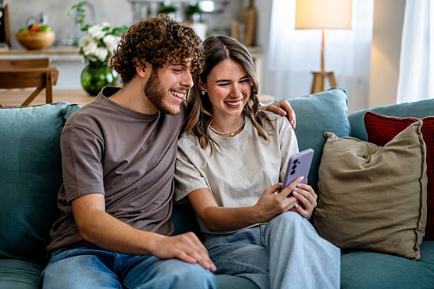 istock Young couple sitting on sofa watching smartphone together 2242838825