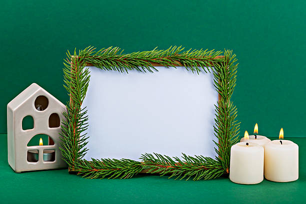 istock Decorative frame with evergreen branches, candles, and ceramic house on green background 2242841605
