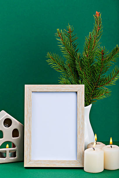 istock Empty wooden frame with candles, evergreen branches, and decorative house on green background 2242842188