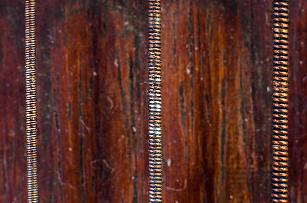 Extreme macro closeup of three copper wrapped strings on dark wooden background showing texture, metallic detail, and vintage craft.