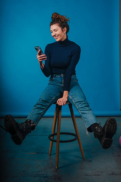 istock A model is sitting on a stool with a smartphone, against a vibrant blue background 2242851493