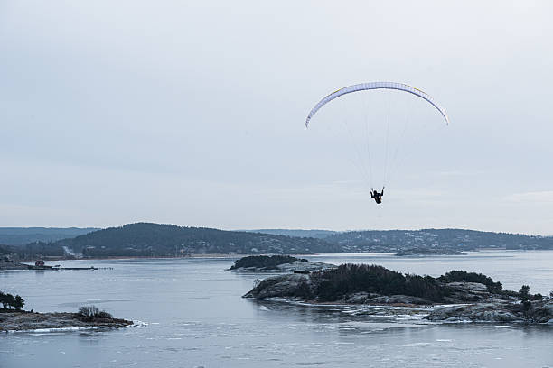 Paraglider soaring above frozen coastal landscape.