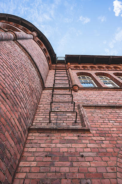 Upward view of red brick building with ladder.