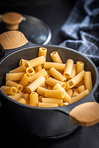 istock Uncooked rigatoni pasta in pot on black table. 2242853287