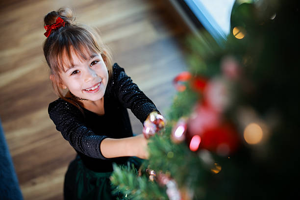 Happy child girl with gift in morning at Christmas tree. Little girl with blond hair sitting on the floor near the Christmas tree and examining different Christmas presents at home