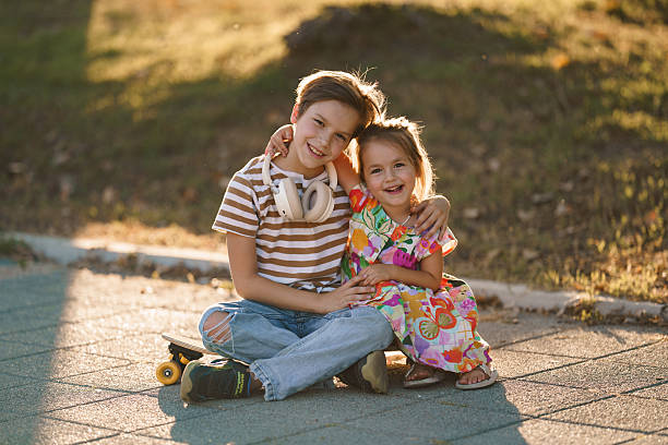 Siblings hugging each other, sitting outdoors on a skateboard, feeling happy and smiling.
