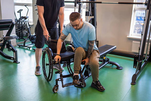 istock Professional sports trainer help disabled man in wheelchair move from exercise machine to wheelchair 2242860843