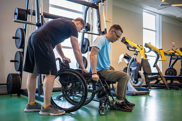 istock Professional sports trainer help disabled man in wheelchair move from exercise machine to wheelchair 2242862529