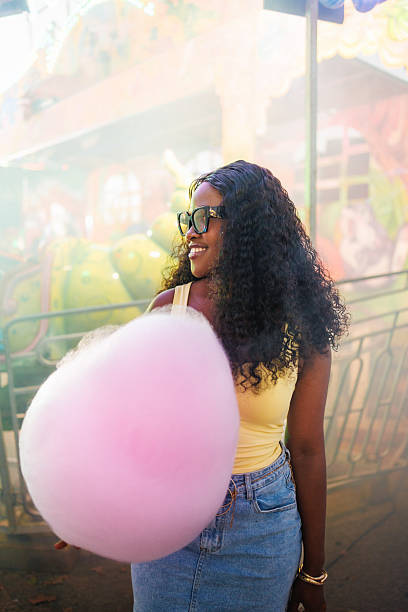 istock Young woman smiling while holding pink cotton candy at a fair 2242864002