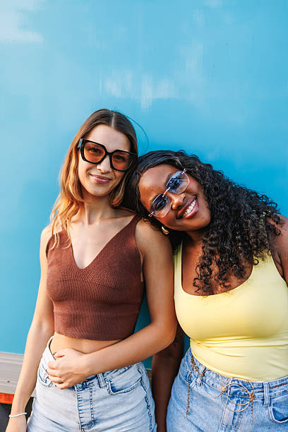 istock Two diverse young women smiling happily while standing leaning on a blue wall 2242866001