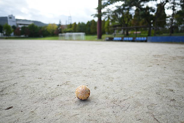 Close-up of petanque precision shooting moment with metal ball hitting target boule, sand and dust flying from impact on gravel court.