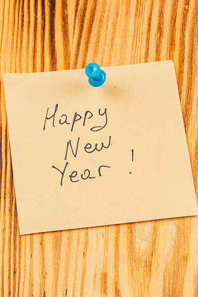istock Bright yellow sticky note with handwritten New Year greeting on wooden surface 2242870647