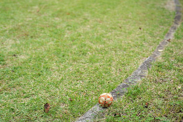 A soccer ball is sitting on the grass next to a line. The grass is dry and brown, and the ball is slightly deflated. The scene gives off a feeling of abandonment and neglect
