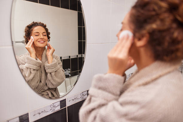 istock Woman cleansing face with cotton pad in bathroom mirror 2242872916