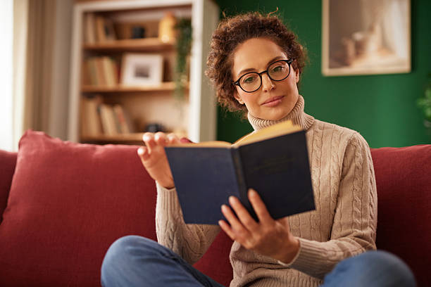 istock Woman reading book relaxing on red couch at home 2242880239
