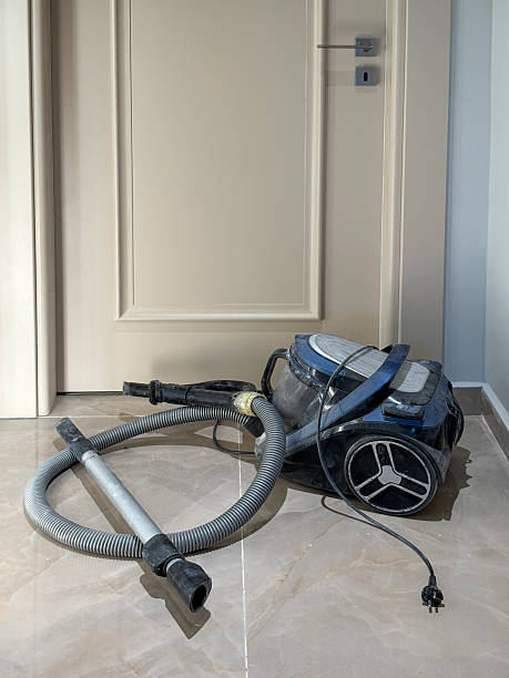 Old and dirty vacuum cleaner in front of the room door on tiled floor at home