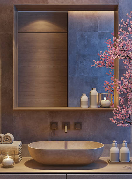 A modern Spa Japandi-style bathroom featuring a floating vanity, round vessel sink, and wall-mounted faucet. The space is softly illuminated by warm LED strip lighting along the ceiling and mirror, creating a calm nighttime ambiance. Natural textures like stone wall finishes and minimalist decor enhance the serene atmosphere. A blooming sakura tree in a planter adds a gentle touch of color and elegance, balancing the neutral tones and clean lines. Night scene.