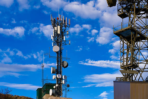 Tall radio tower antenna on mountaintop with multiple communications equipment mounted against blue sky and clouds.