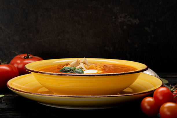 Close-up of hot vegetable soup in a yellow bowl with spoon, served on dark rustic table. Warm homemade meal.