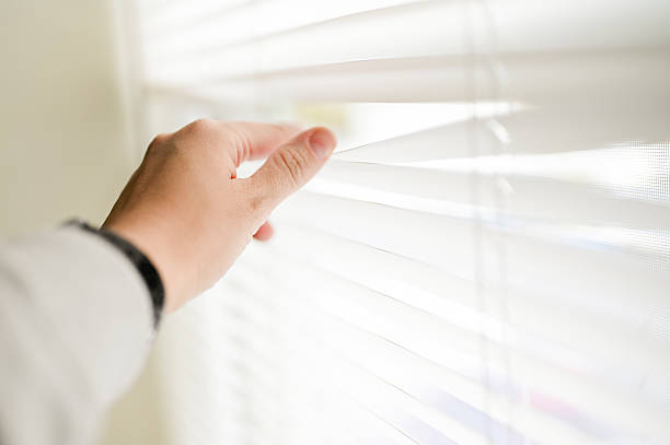 istock Hand opening white window blinds to look outside 2242904191