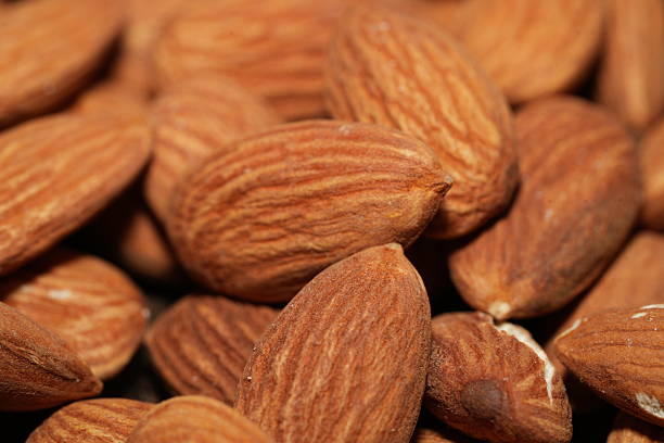 Close-up photo of almonds highlighting their matte brown skin, wrinkled texture, and organic curvature. A tactile study in natural design and the sculptural beauty of nutritious food.