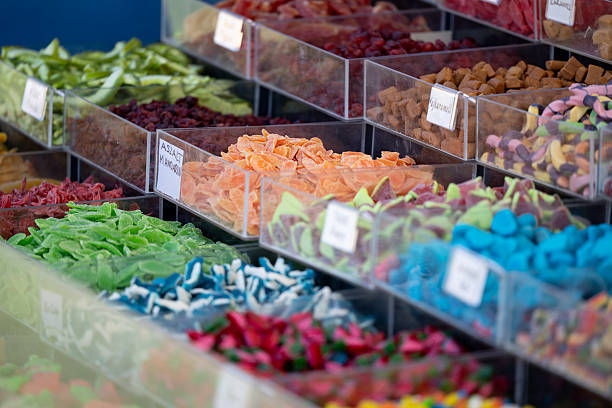 A vibrant display of assorted candies arranged in clear plastic containers at a market stall. The mix of bright colors and various shapes creates a cheerful and inviting scene that captures the playful essence of sweets and confectionery.