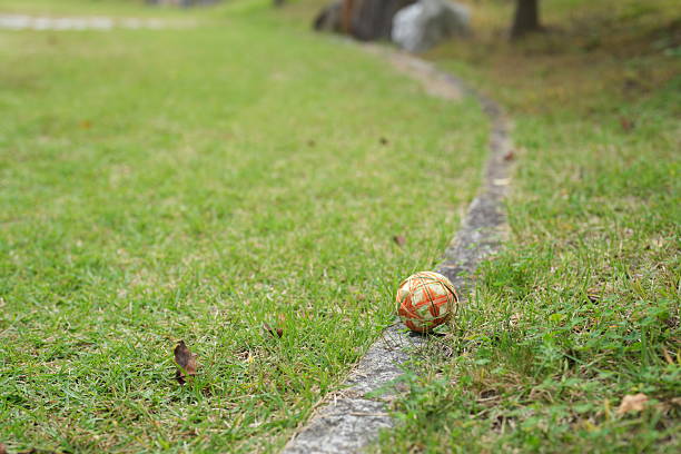 A soccer ball is sitting on the grass next to a stone path. The ball is slightly deflated and he is old. The scene is peaceful and quiet, with the grass and the stone path creating a serene atmosphere