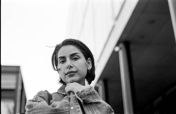 istock Young woman pulling denim jacket while posing in urban setting, grainy monochrome film aesthetic 2242913872