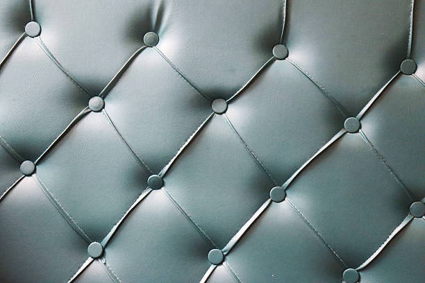 An extreme close-up reveals the intricate texture of tufted teal upholstery. Diamond-shaped patterns are formed by precise stitching and small, dark buttons, creating a rich, tactile surface perfect f
