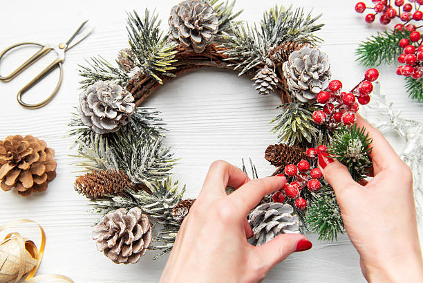 istock Hands decorating christmas wreath with pine cones and evergreen 2242926004