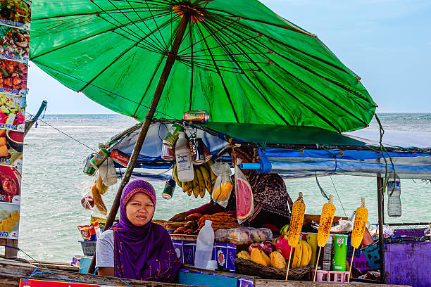 Krabi Province, Thailand - January 11, 2014: Woman selling snacks at beachside stall under large green umbrella, beach Phra Nang in Thailand