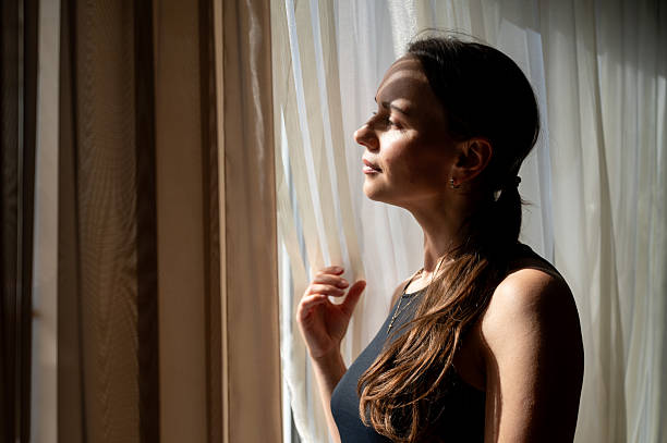 istock Thoughtful woman looking out the window in sunlight, cozy interior 2242936982