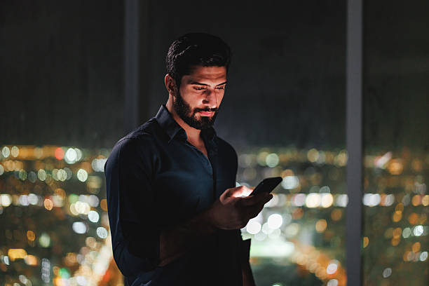 istock Young Arabic Businessman Using Smartphone in Modern Hotel Room Overlooking Riyadh Cityscape 2242939911