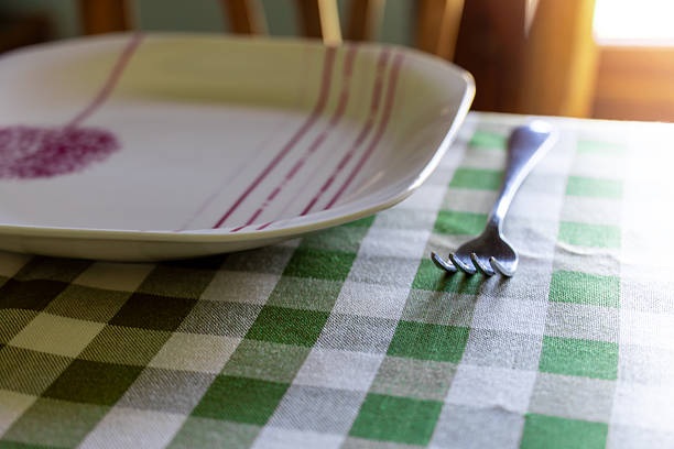 A fork and an decorated dish are on a green and white checkered tablecloth. Warm light comes in through the window